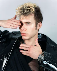 a young man in a black leather jacket posing with his hands on his face